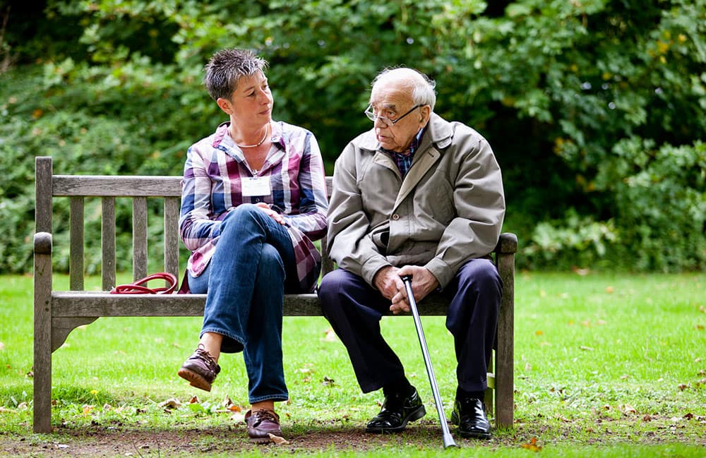 Älterer Mann und Frau sitzen auf einer Parkbank.