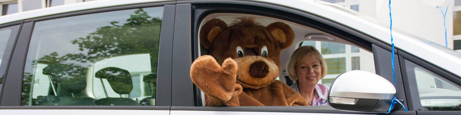 Mensch im Bärenkostüm winkt aus dem Beifahrer-Autofenster
