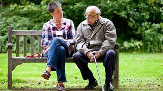Eine jüngere Frau und ein älterer Mann im Gespräch auf einer Parkbank